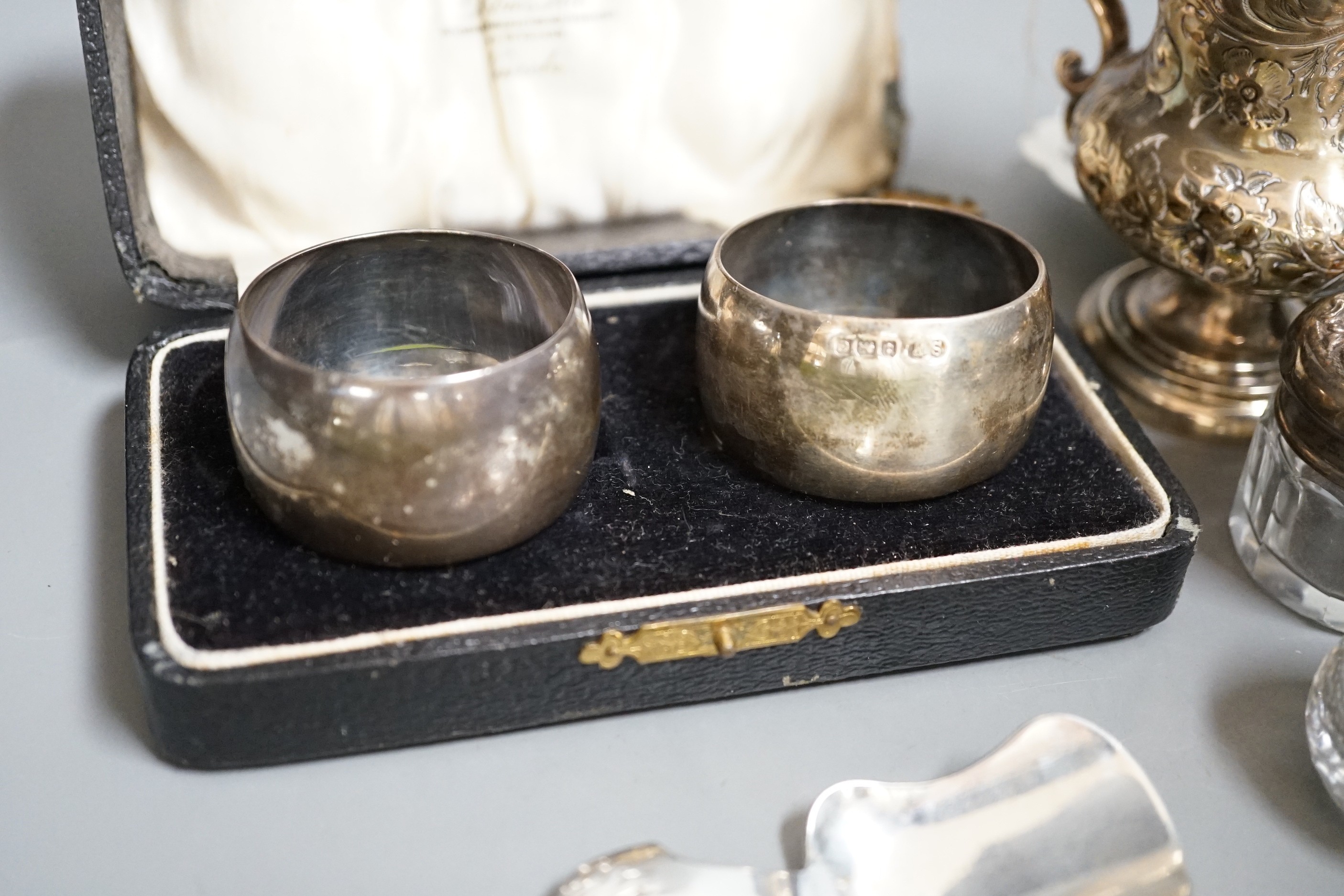 A Victorian repousse silver christening mug, Birmingham, 1861, 9.5cm, a cased pair of silver napkin rings, four assorted silver mounted toilet jars, a silver compact, small silver trophy cup and a silver caddy spoon.